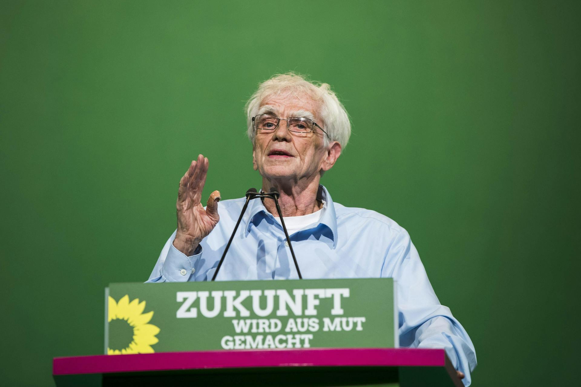 Hans-Christian Ströbele steht hinter einem Redner*innenpult mit der Aufschrift "Zukunft wird aus Mut gemacht"
