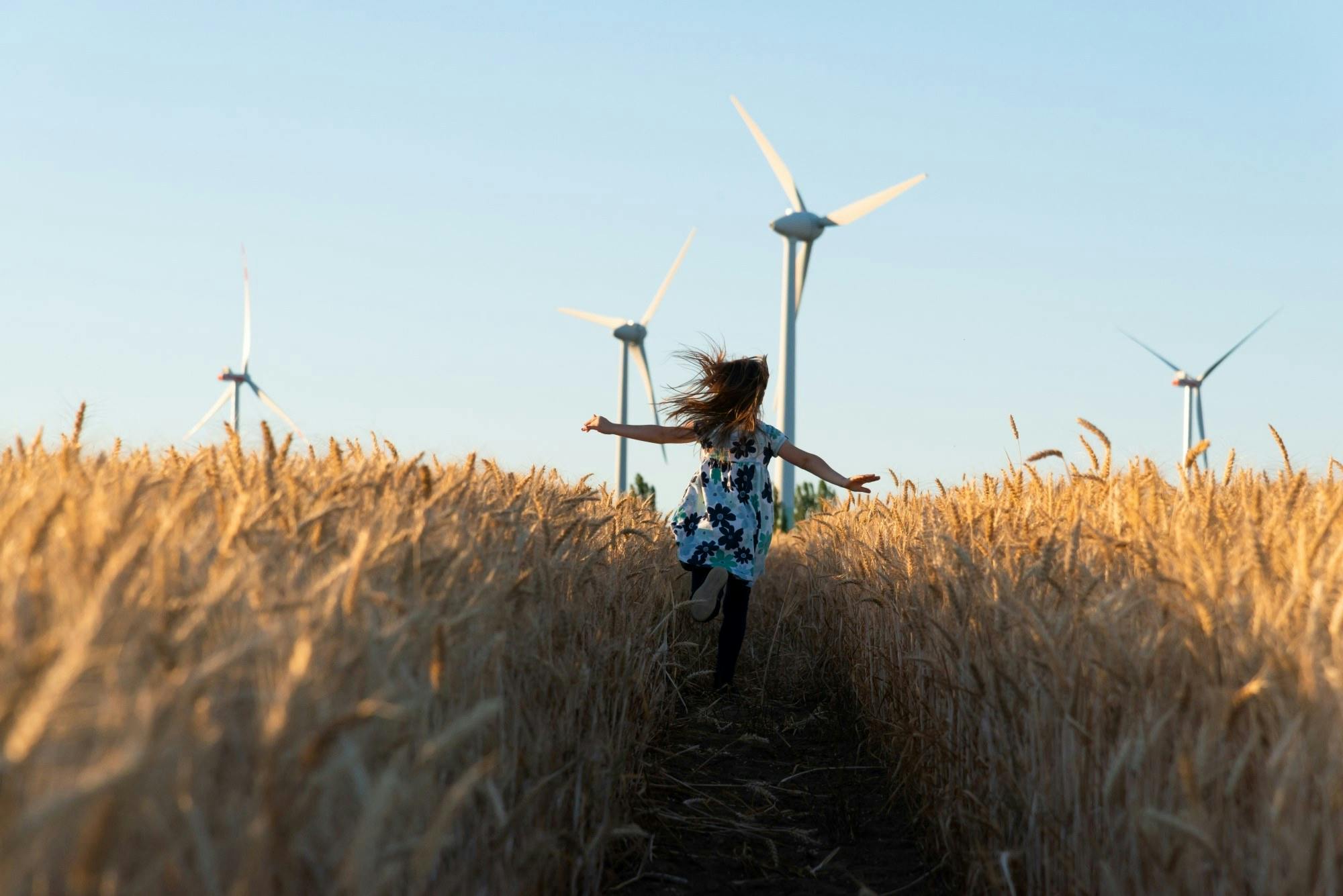 Kind rennt ueber Feld mit Windkraftanlagrn