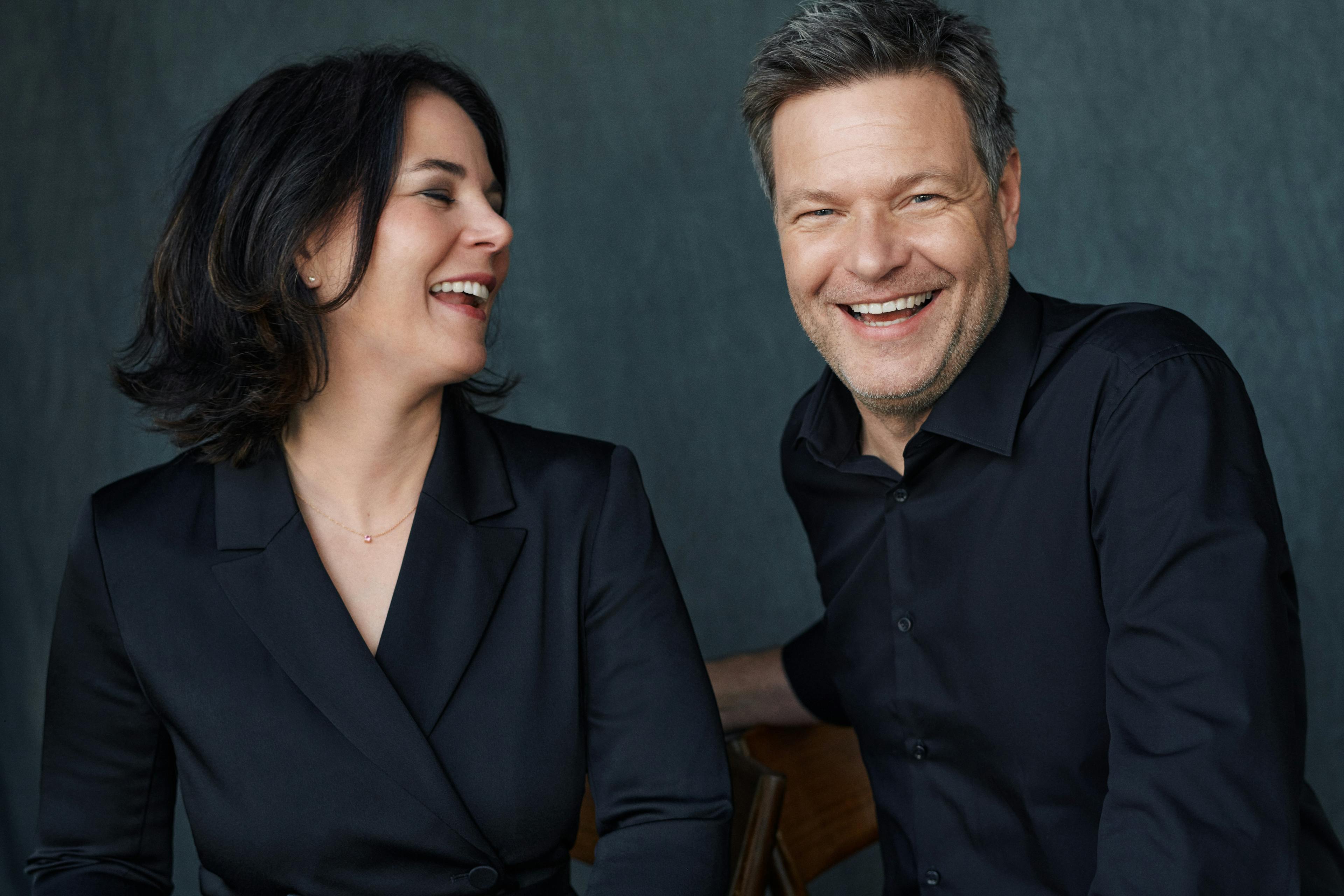 Robert Habeck (links) und Annalena Baerbock sitzen nebeinander und lachen. Beide tragen schwarz.